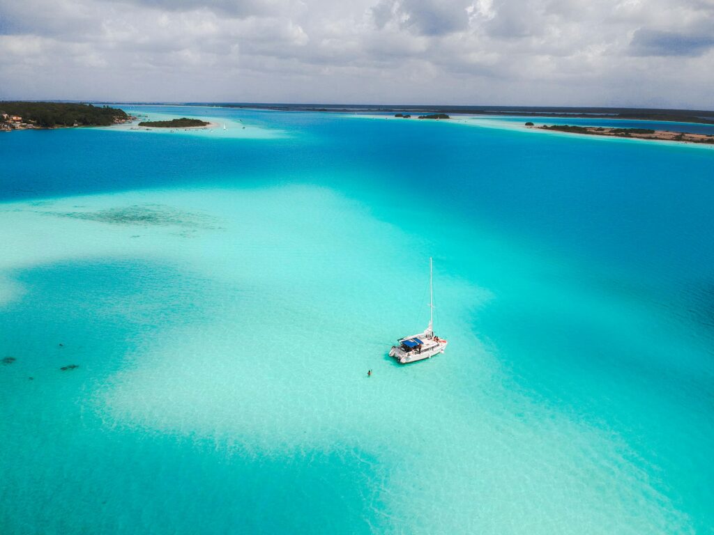 Bacalar: el paraíso barato que parece Maldivas mexicanas (guía real) A stunning aerial view of a sailboat in the tranquil turquoise waters of Bacalar Lagoon, Mexico.